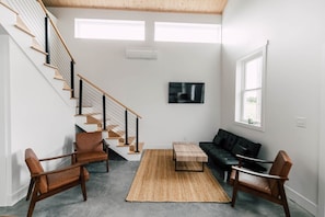 A modern living room with a staircase, a sofa, two chairs, a coffee table, and a TV.