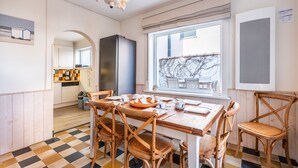 A dining area with a checkered floor, wooden chairs, a table set for four, and a window with a view of a building and trees. - Villa Near Belgian Coast With Sea Views (Koksijde)
