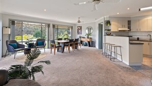 A spacious living area with a dining table, chairs, and a kitchen area with bar stools. - Sapphire Belle: Views and boat Parking (Eden)