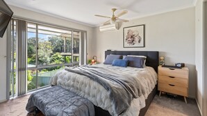 A bedroom with a large bed, a ceiling fan, a nightstand, and a view of greenery through a sliding door. - Sapphire Belle: Views and boat Parking (Eden)