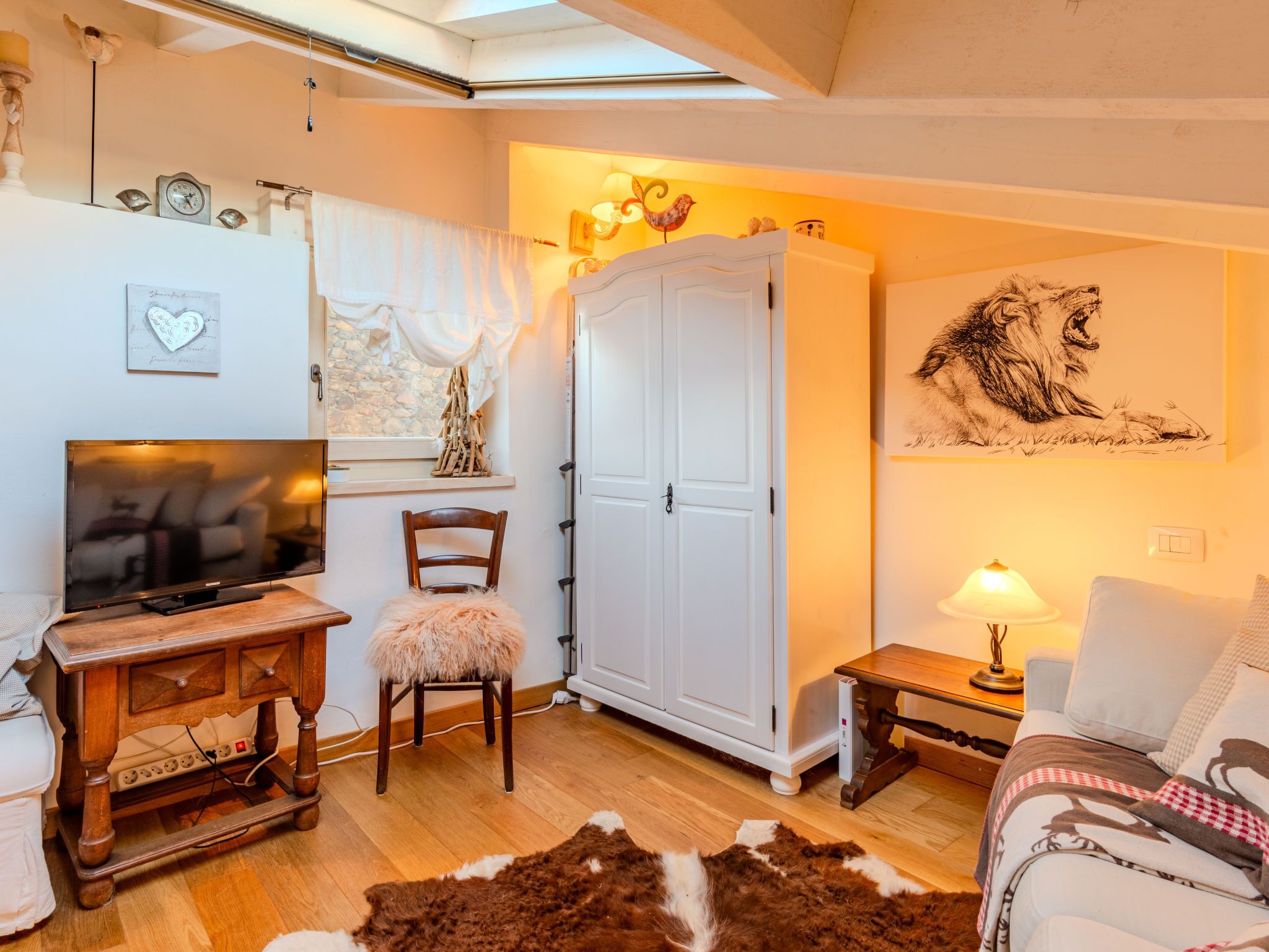 Ein gemütliches Wohnzimmer mit Fernseher, Holzmöbeln, einem weißen Kleiderschrank und einem Kuhfellteppich.