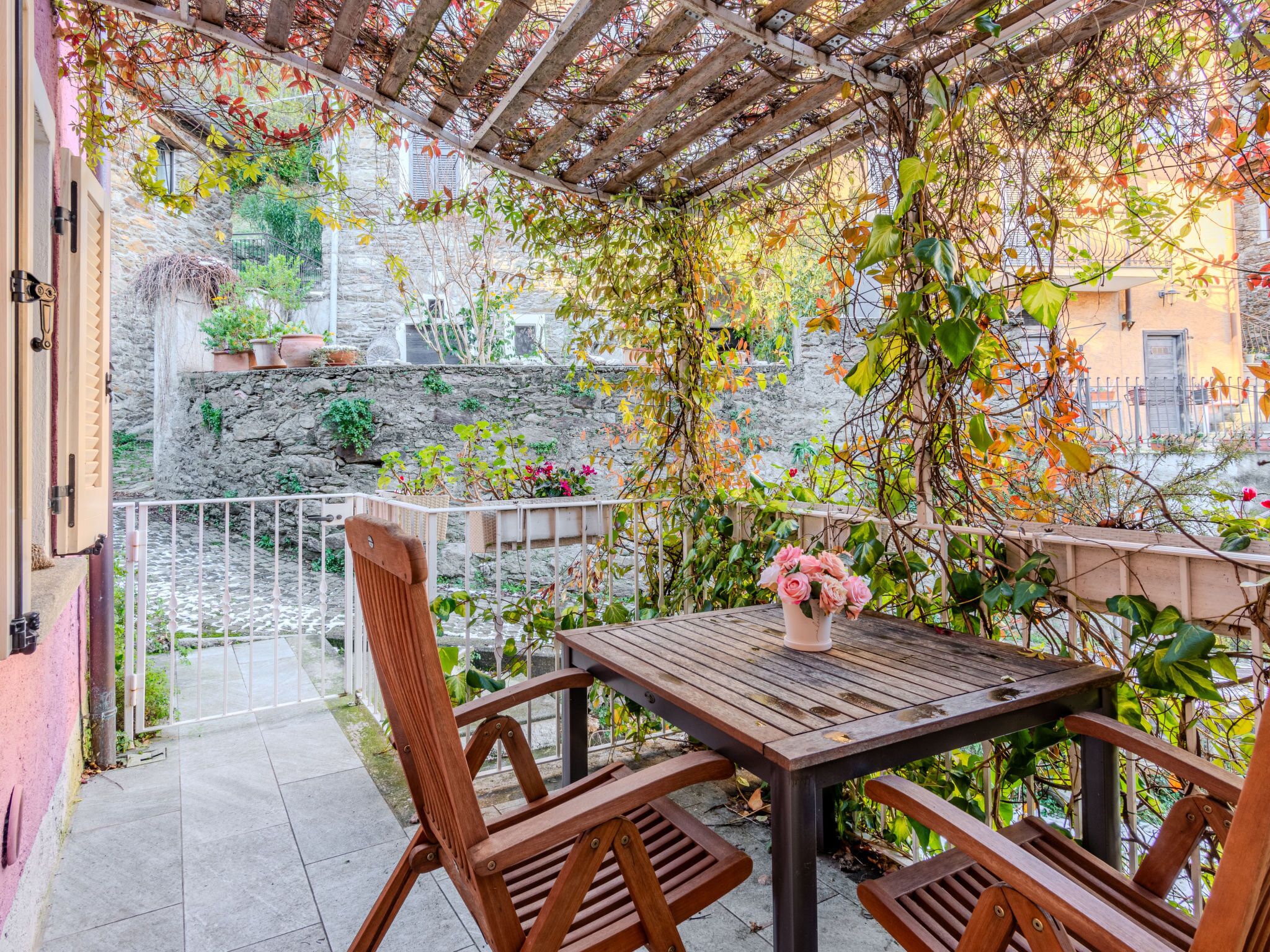 A wooden table with chairs, surrounded by plants and a stone wall.