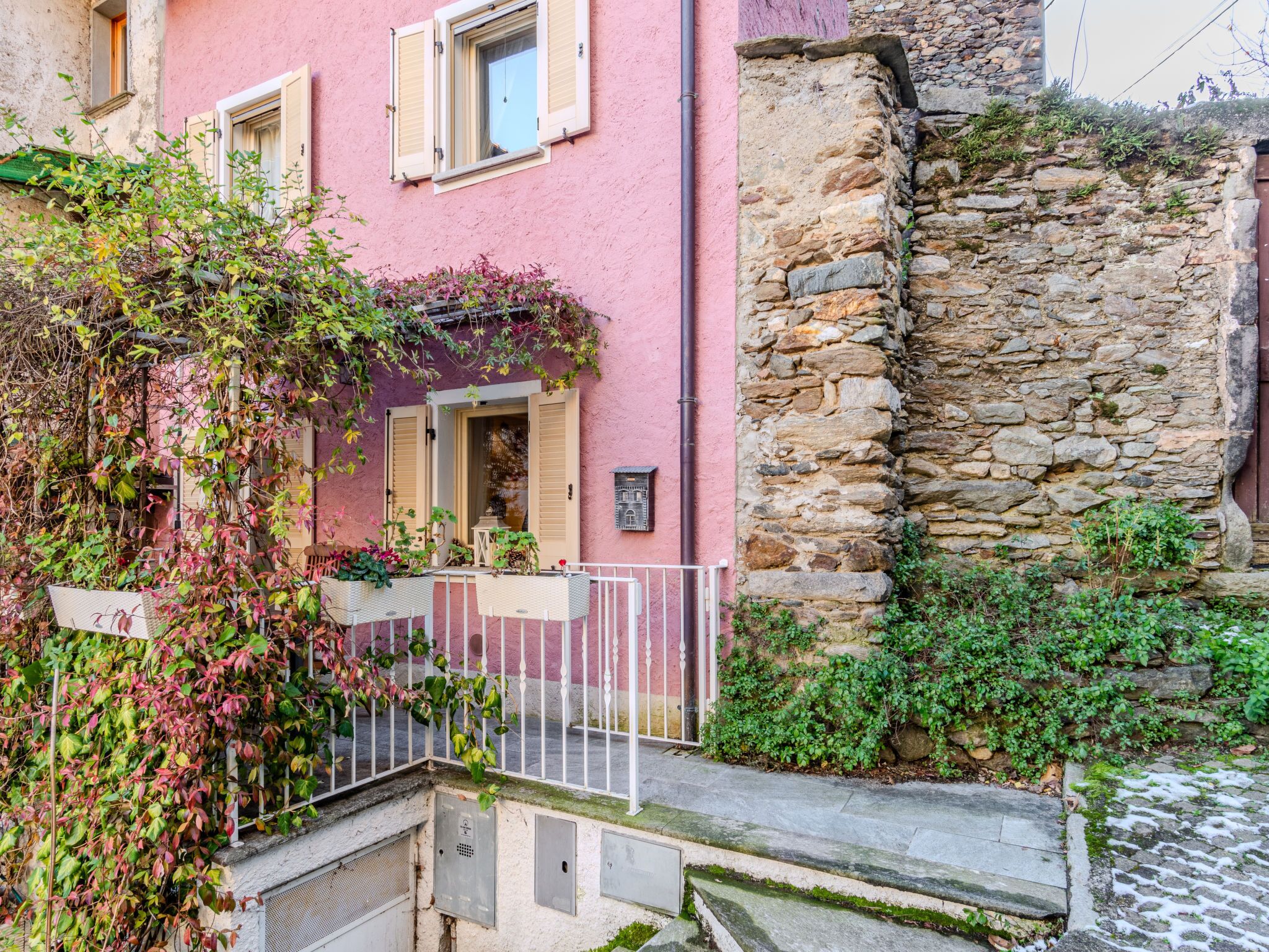 A pink building with a stone wall, a metal gate, and a staircase leading to a door.