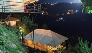 Une structure en forme de tente, dotée d’une plateforme et d’une rambarde, et entourée de verdure.