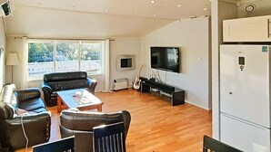 A living room with a sofa, a coffee table, a TV, a guitar, and a refrigerator. - 6 Person Holiday Home in Hosteland (Masfjorden)