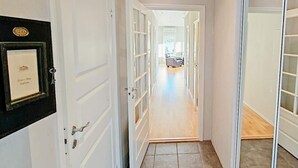 A hallway with white doors, a framed certificate on the left, and a glimpse of a living area with a sofa and a window at the end. - 6 Person Holiday Home in Hosteland (Masfjorden)