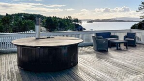 A wooden deck with a round table and chairs, overlooking a body of water and hills. - 6 Person Holiday Home in Hosteland (Masfjorden)
