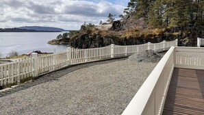 A gravel path with a white fence and a wooden deck overlooking a body of water and a forested area. - 6 Person Holiday Home in Hosteland (Masfjorden)