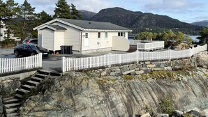 A small, single-story cabin with a white exterior, a porch, and a stone retaining wall. - 6 Person Holiday Home in Hosteland (Masfjorden)