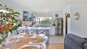 Een moderne keuken met witte kasten, een roestvrijstalen koelkast en een eethoek met een houten tafel en geweven placemats.
