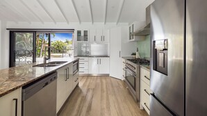 Een moderne keuken met witte kastjes, roestvrijstalen apparatuur en een groot raam met uitzicht op een terras.