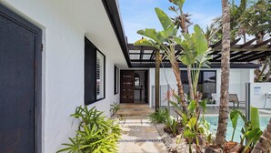 Een modern huis met een overdekt terras, een zwembad en tropische planten.