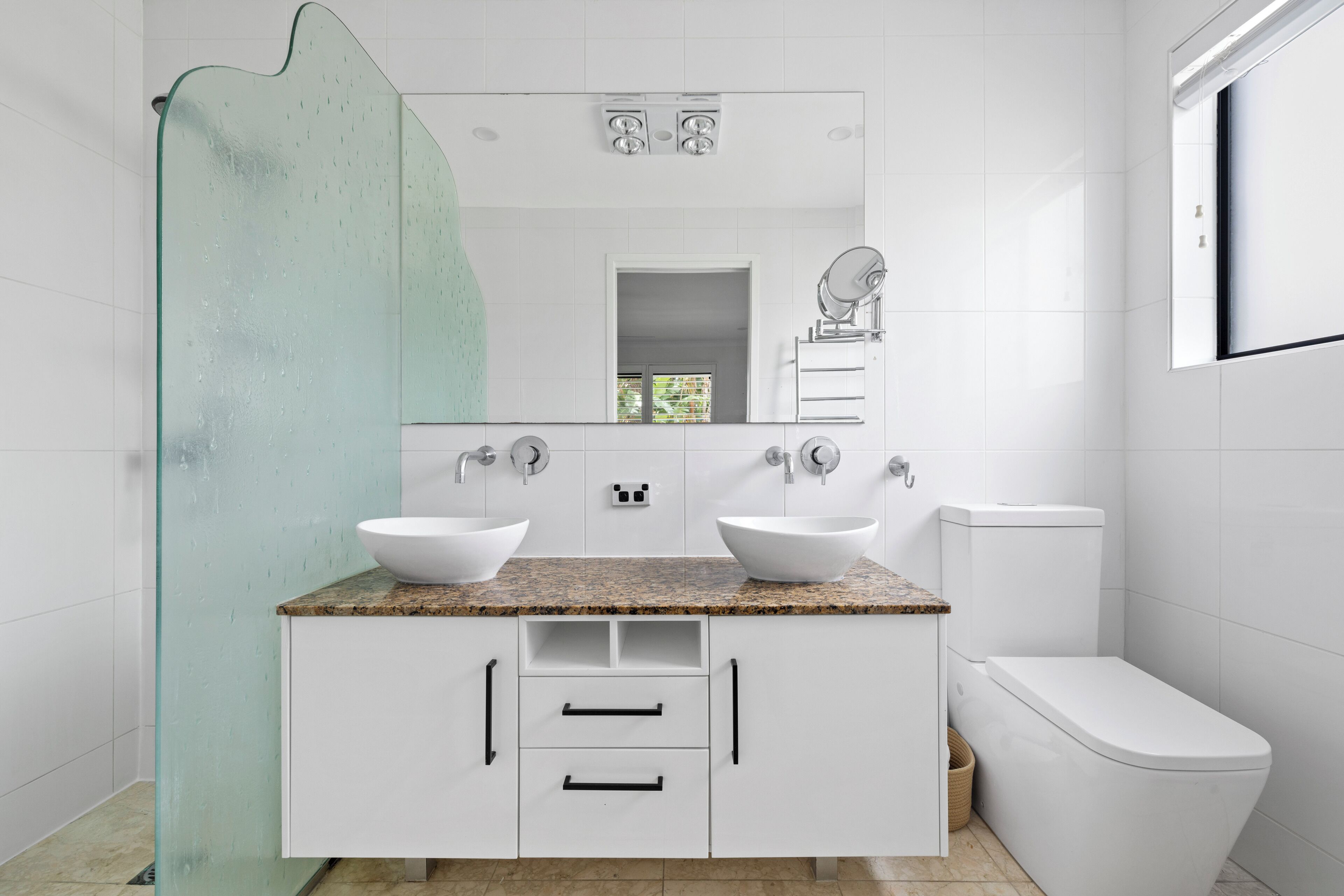 A modern bathroom with two sinks, a toilet, and a shower enclosure.