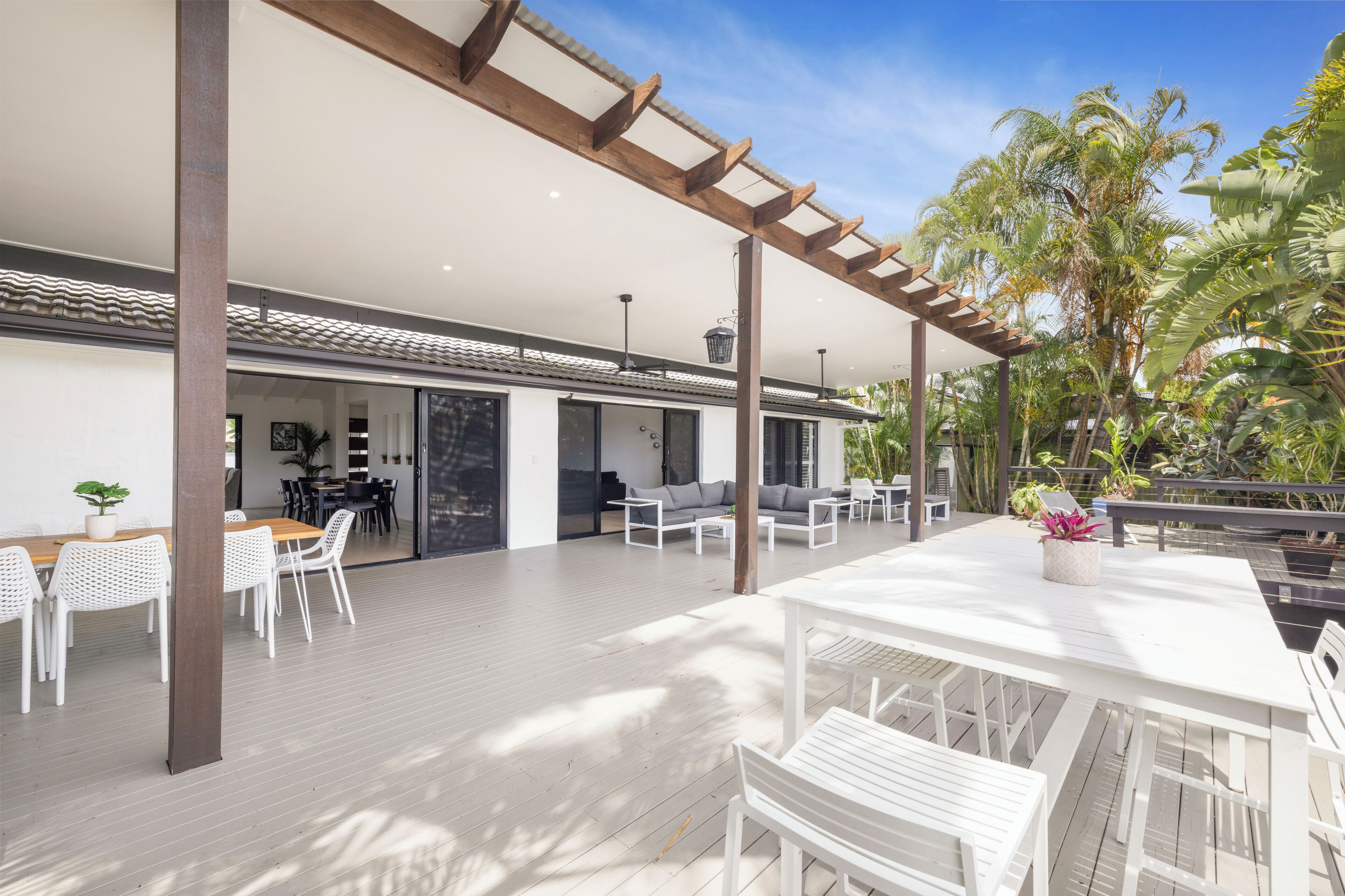 An open-plan living area with a wooden deck, white furniture, and a view of the outdoors.