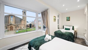 A hotel room with two beds, a large window with a view of a church and a building, and a small bedside table with a lamp. - 5 Bedroom Oxford Cooper House, Sleep 11, Parking (Oxford)