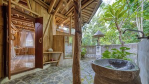 Una habitación rústica de madera con suelo de piedra, un lavabo de piedra grande y vistas a un jardín exuberante.