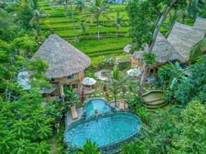 A resort with a swimming pool, thatched-roof buildings, and lush greenery. - Bamboo Cabin Sanctuary Ubud (Ubud)