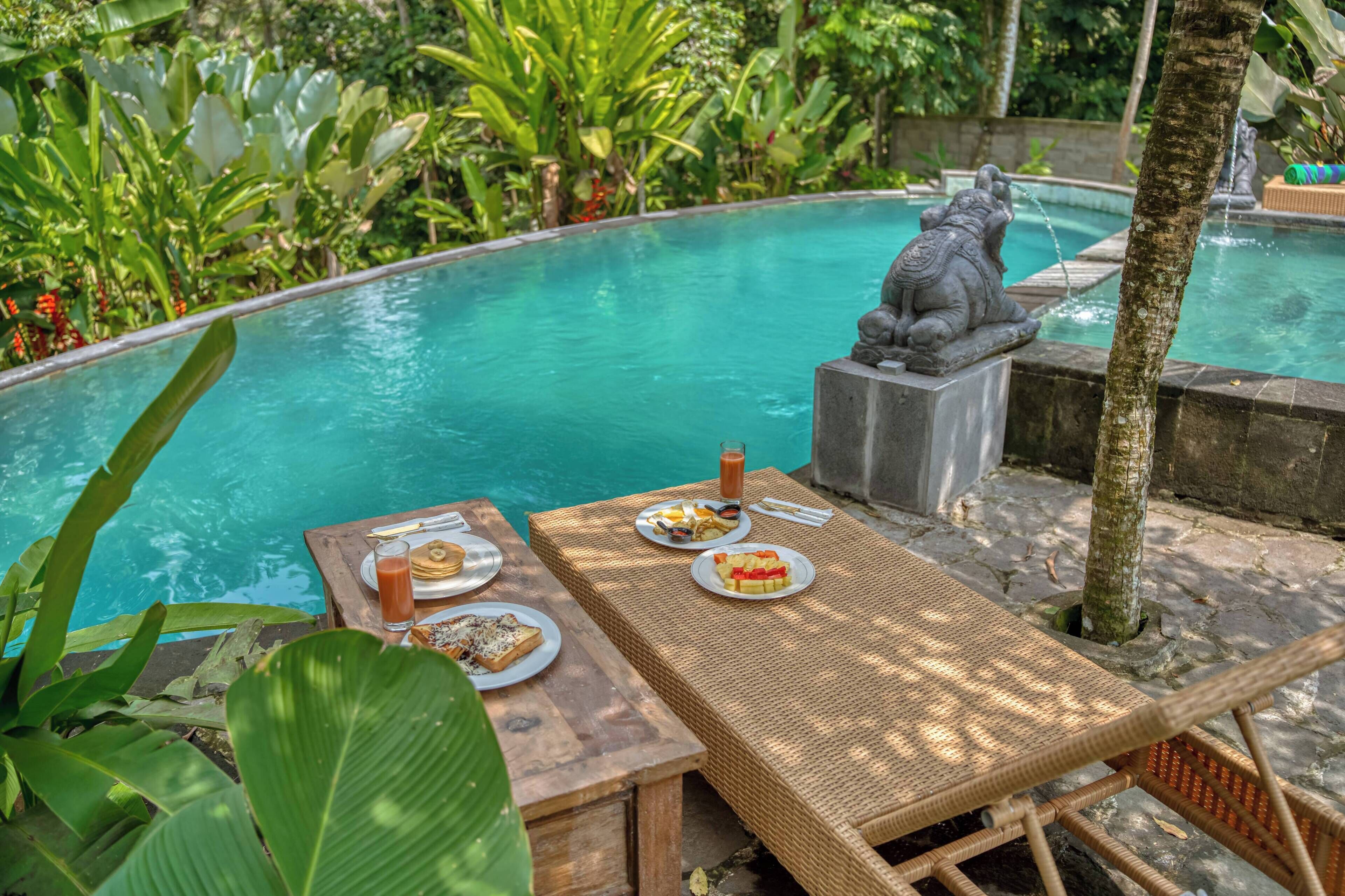 A poolside dining area with tables, chairs, and a statue.