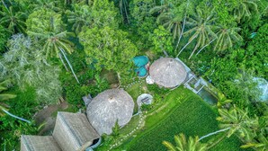 Vista aérea de un resort tropical con cabañas de techo de paja, una piscina y abundante vegetación.