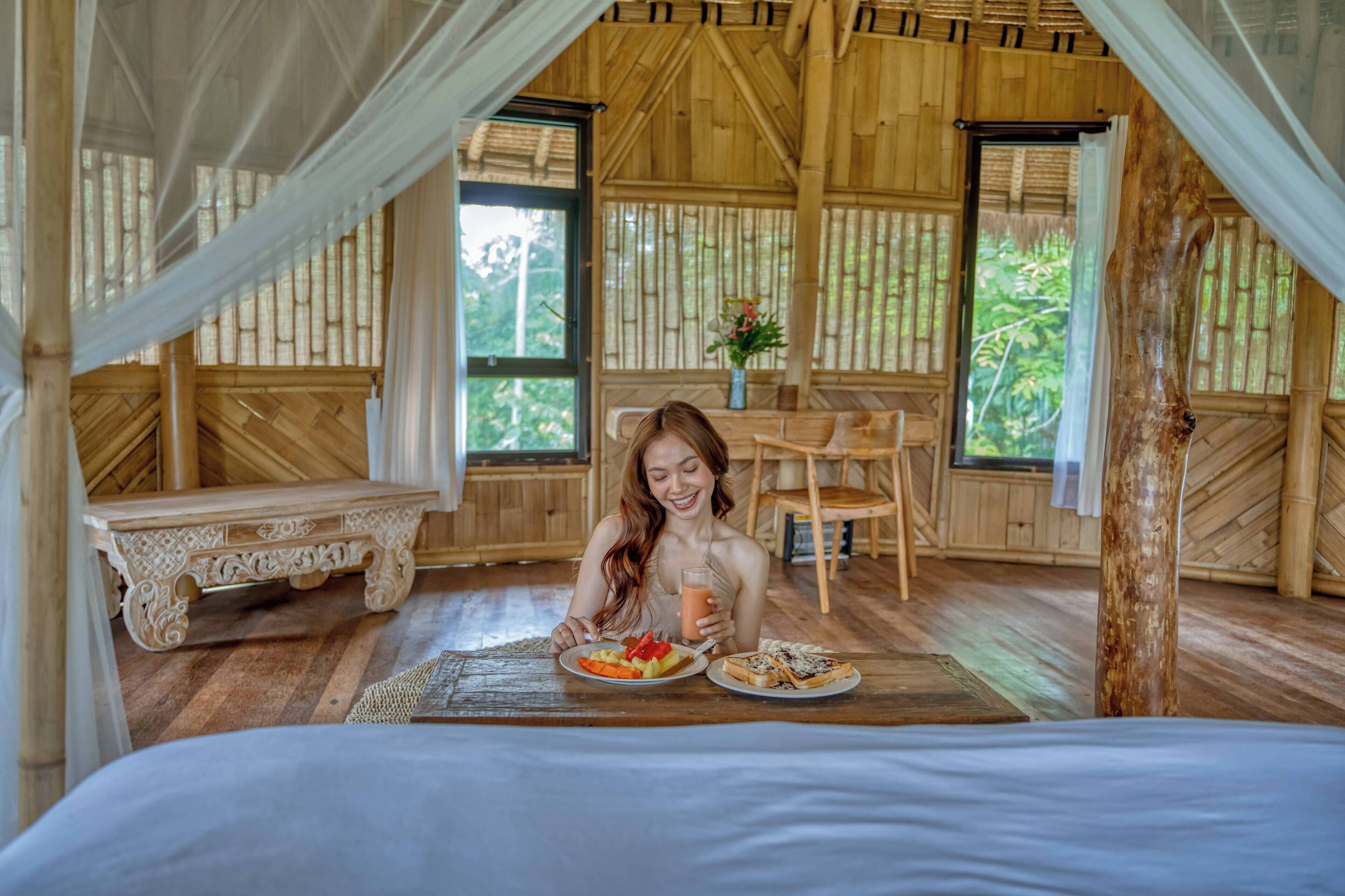A wooden room with a bed, a dining table with food, and a chair.