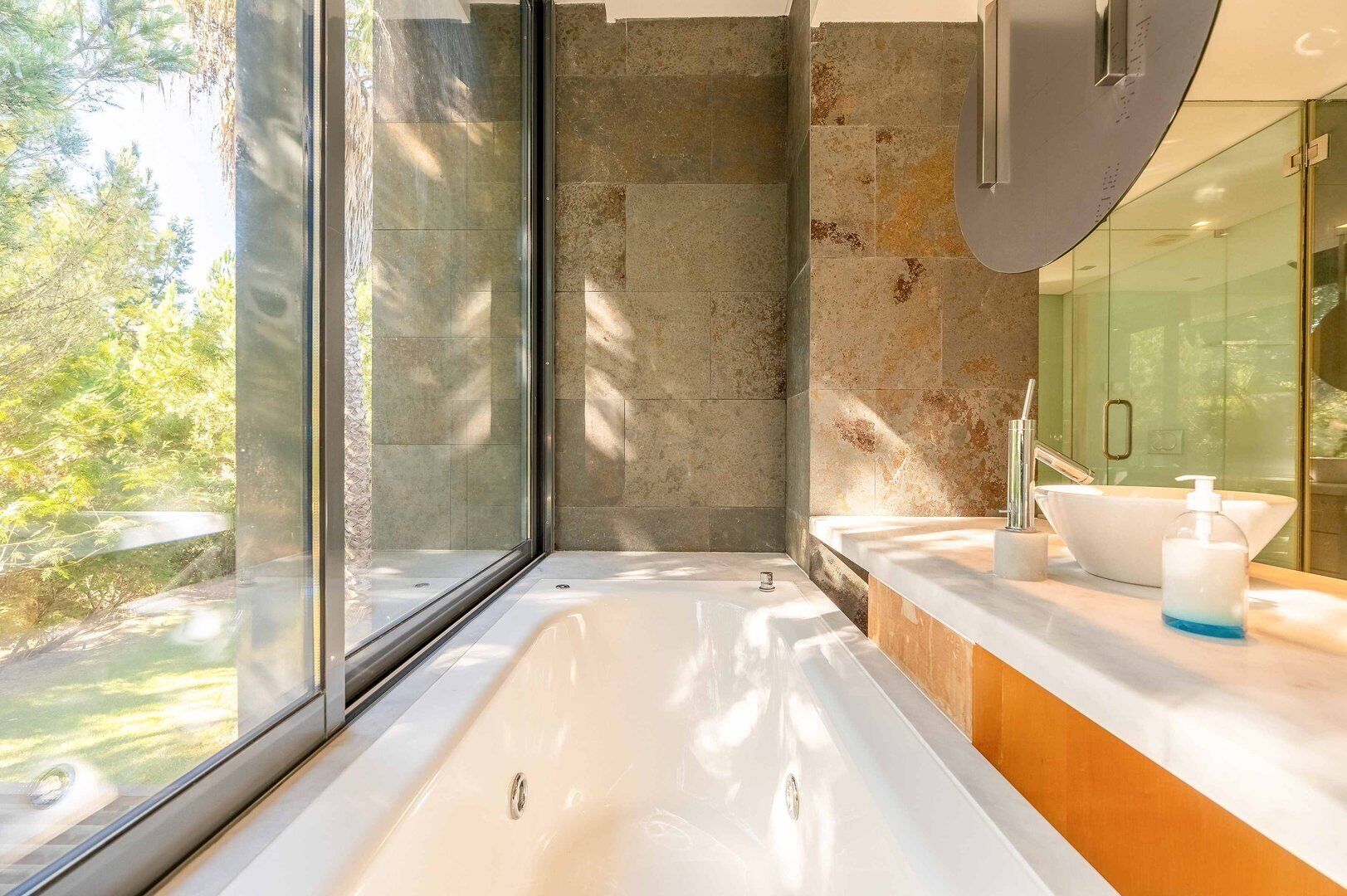 A modern bathroom with a large bathtub, a glass shower enclosure, and a sink with a mirror.