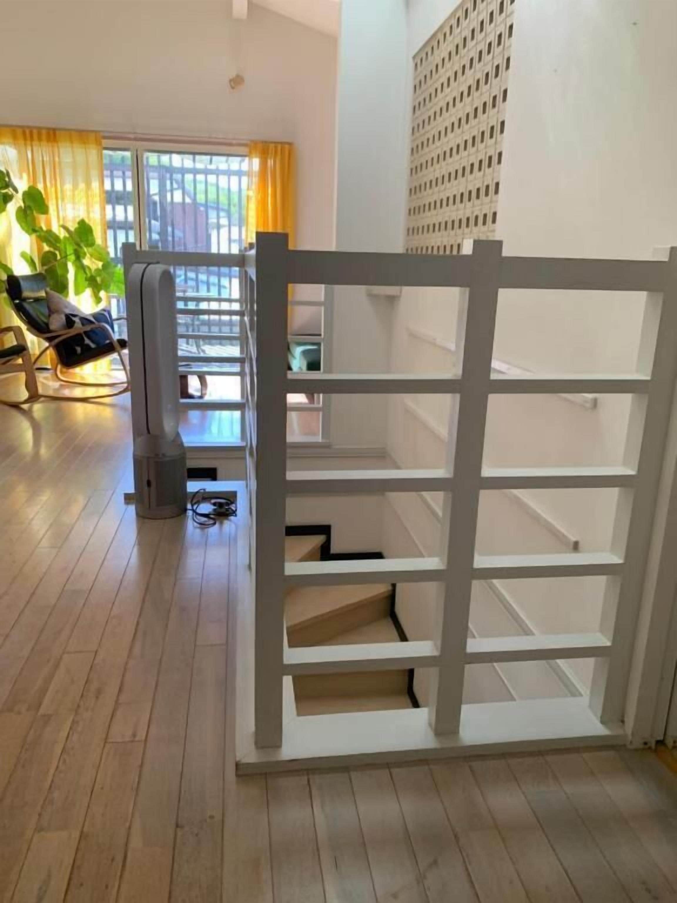 A room with a wooden floor, a white shelf unit, a chair, and a plant.