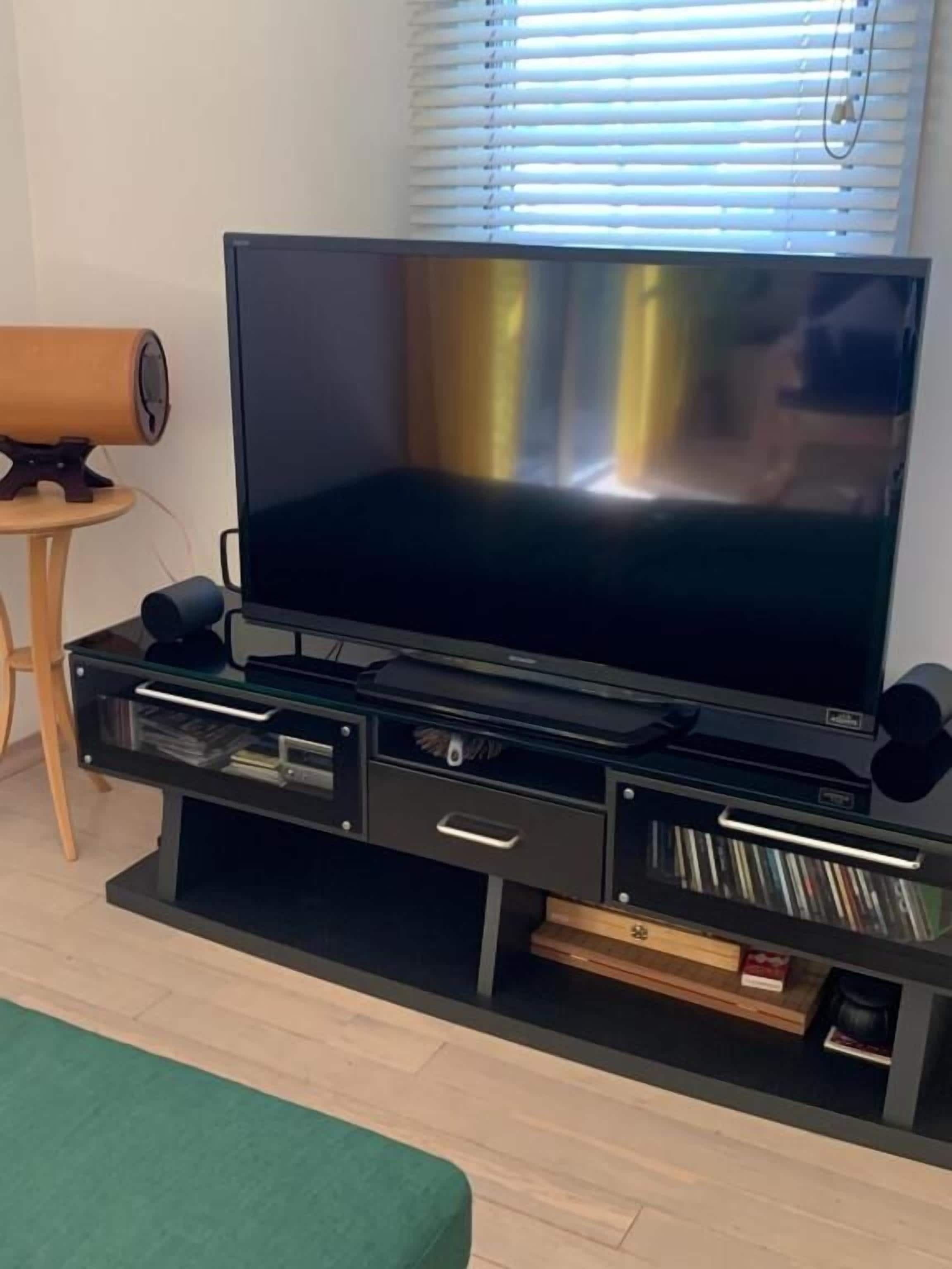A modern living room with a large flat-screen TV on a black entertainment unit, a wooden side table, and a green sofa.
