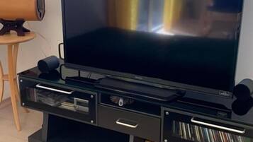 A modern living room with a large flat-screen TV on a black entertainment unit, a wooden side table, and a green sofa.