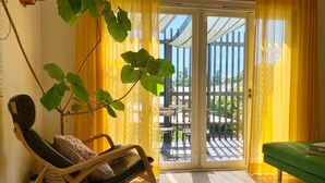 A room with a sliding glass door leading to an outdoor patio, a rocking chair, a green sofa, and a potted plant. - Kamakura Vacation House (Kamakura)