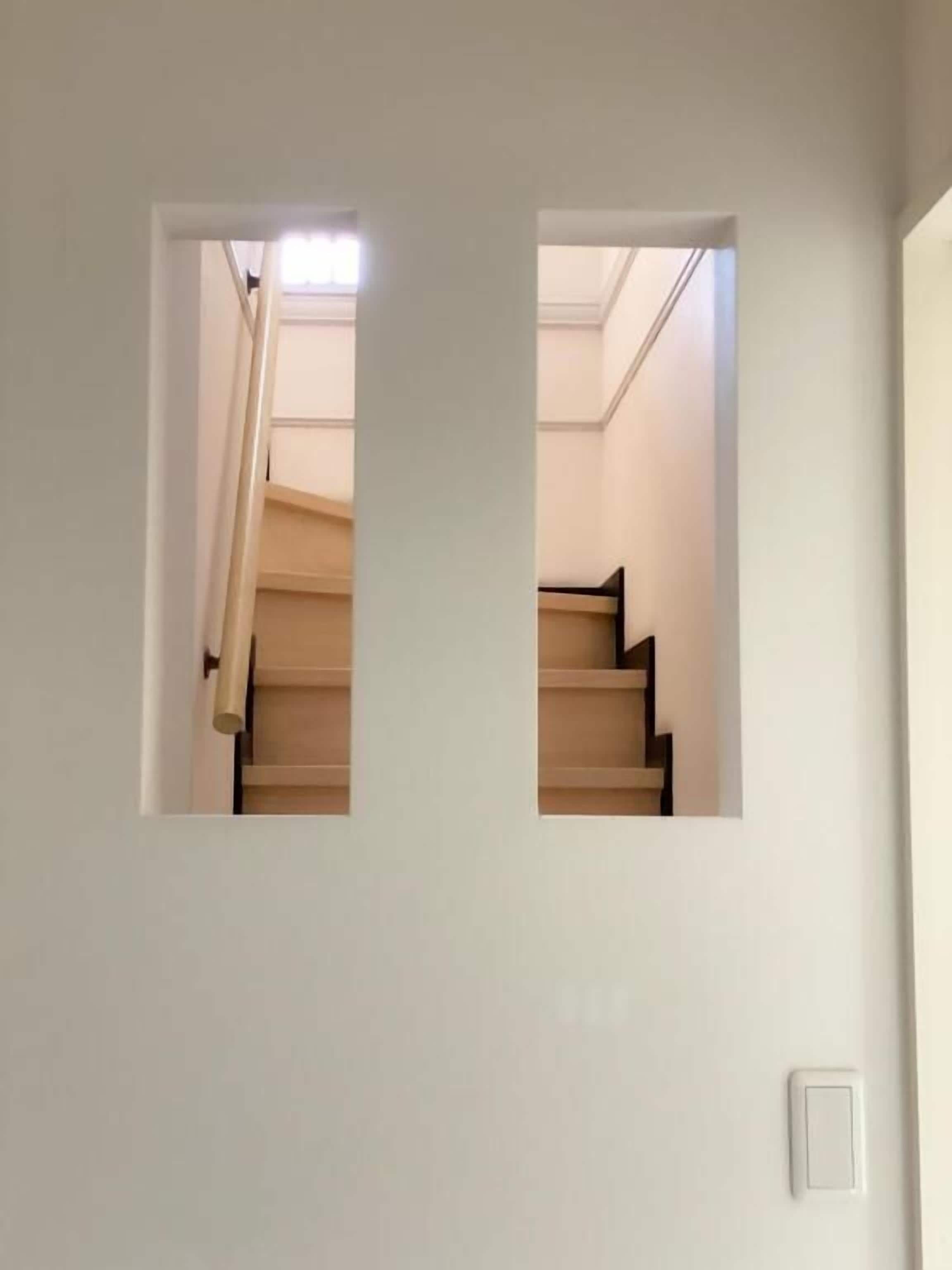 A staircase with wooden steps and a beige handrail, leading to a landing with a light switch on the wall.