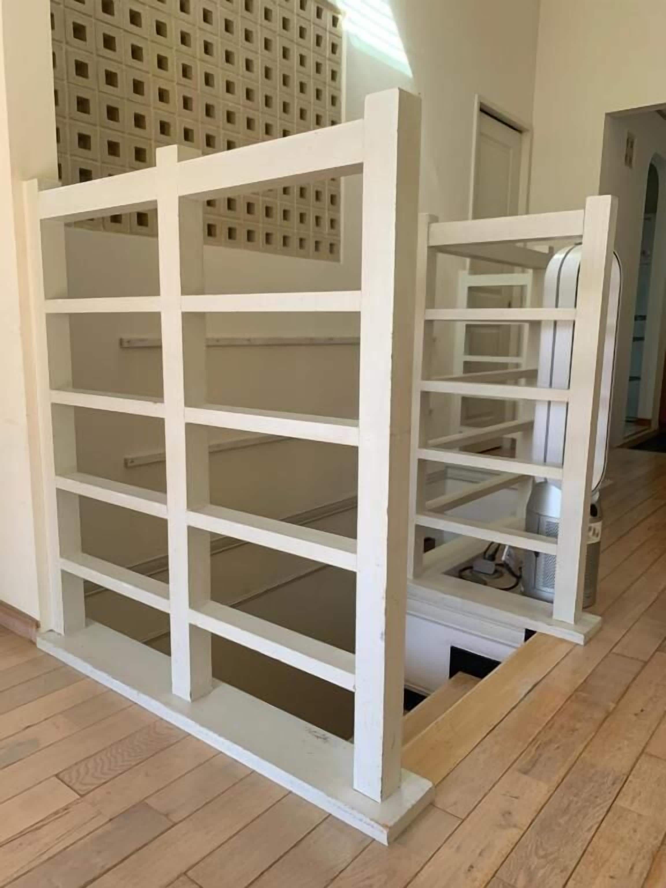 A white metal rack with multiple shelves, likely for storage, in a room with wooden flooring and a white door in the background.