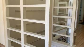 A white metal rack with multiple shelves, likely for storage, in a room with wooden flooring and a white door in the background.