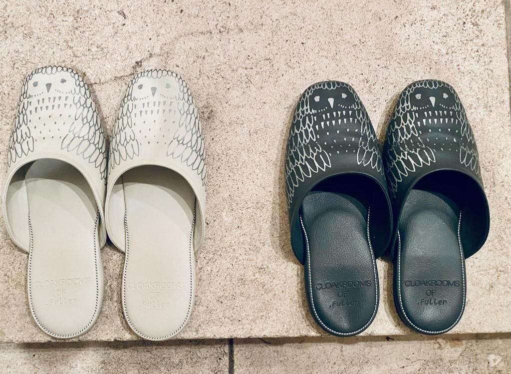 Un par de pantuflas blancas y negras con un estampado de cocodrilo, sobre una superficie texturizada.