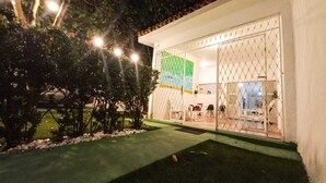 Un edificio bien iluminado con un espacio al aire libre cubierto, un césped verde y una valla.