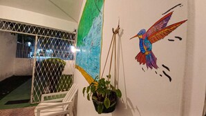 Habitación con un mural de un colibrí, una planta colgante y una ventana con reja de metal.