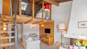 A cozy room with a loft bed, a sofa, a TV, and a dining area with a table set for two.