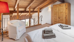 A bedroom with a wooden ceiling, a white bed, a red lamp, a wooden wardrobe, and a balcony with a view.