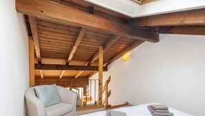 Un dormitorio con techo de madera, un sofá, una cama con toallas y una escalera.