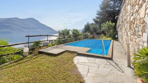 Piscina con muro de piedra y vista a un lago y montañas.
