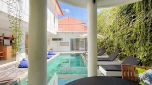 A poolside area with a clear view of a swimming pool, lounge chairs, and a building with a red roof in the background. - 3BR Del Mar Tropical Villa 4 in Seminyak Beach (Seminyak)