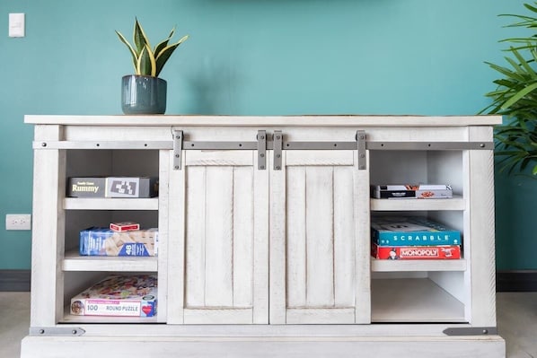 A white cabinet with sliding doors, holding board games like Scrabble and Monopoly.