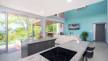 A modern kitchen with a large island, a built-in stove, and a view through large windows.