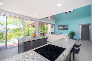 A modern kitchen with a large island, a built-in stove, and a view through large windows.