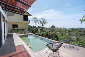A modern house with a rooftop pool, two chairs, and a view of the countryside.