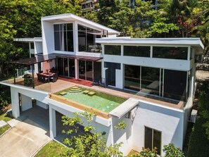 A modern two-story house with a rooftop swimming pool, large windows, and a patio area.