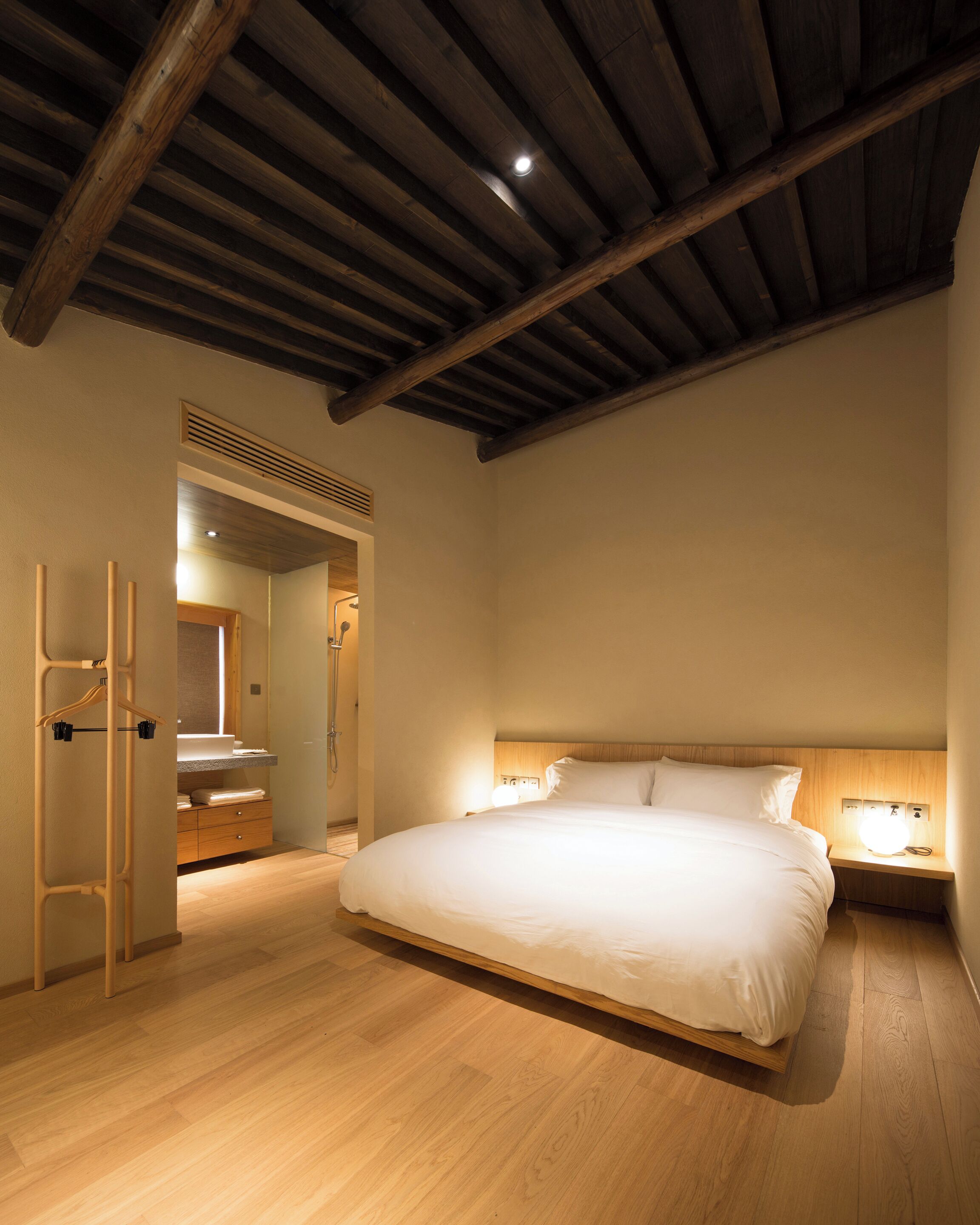 Un dormitorio con una cama grande, vigas de madera en el techo, un armario de madera y una mesita de noche con una lámpara.