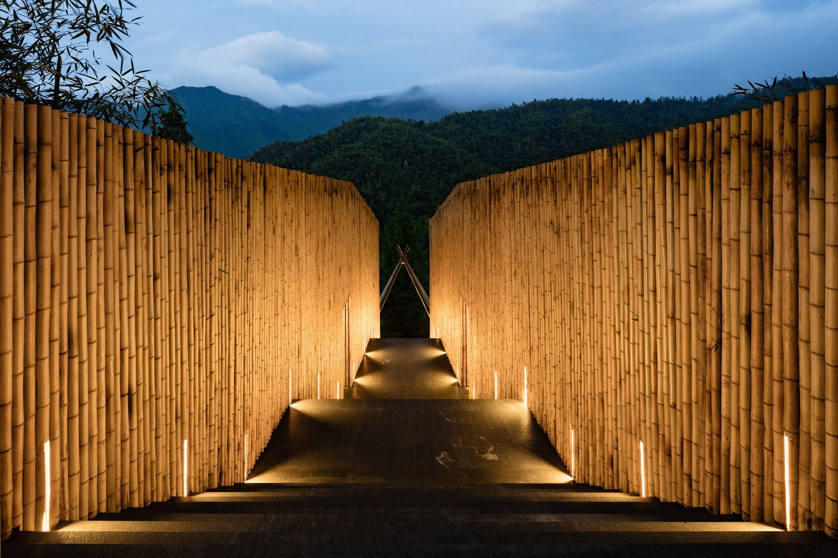 A corridor with bamboo walls and a central pathway leading to a structure.
