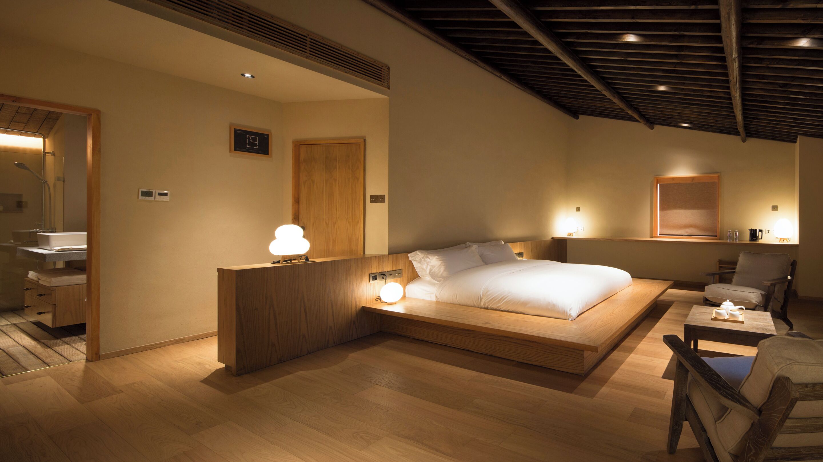 Une chambre à coucher avec un lit en bois, des lampes de chevet, une table de chevet en bois, une chaise et une petite table sur laquelle se trouve une théière.