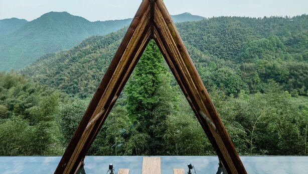 A wooden structure with a reflective floor leading to a seating area with benches and tables, overlooking a forested mountain range. - Origin Villa Hotel (Hangzhou)