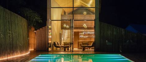 A modern building with a glass facade, a pool in front, and a staircase leading to the upper level.